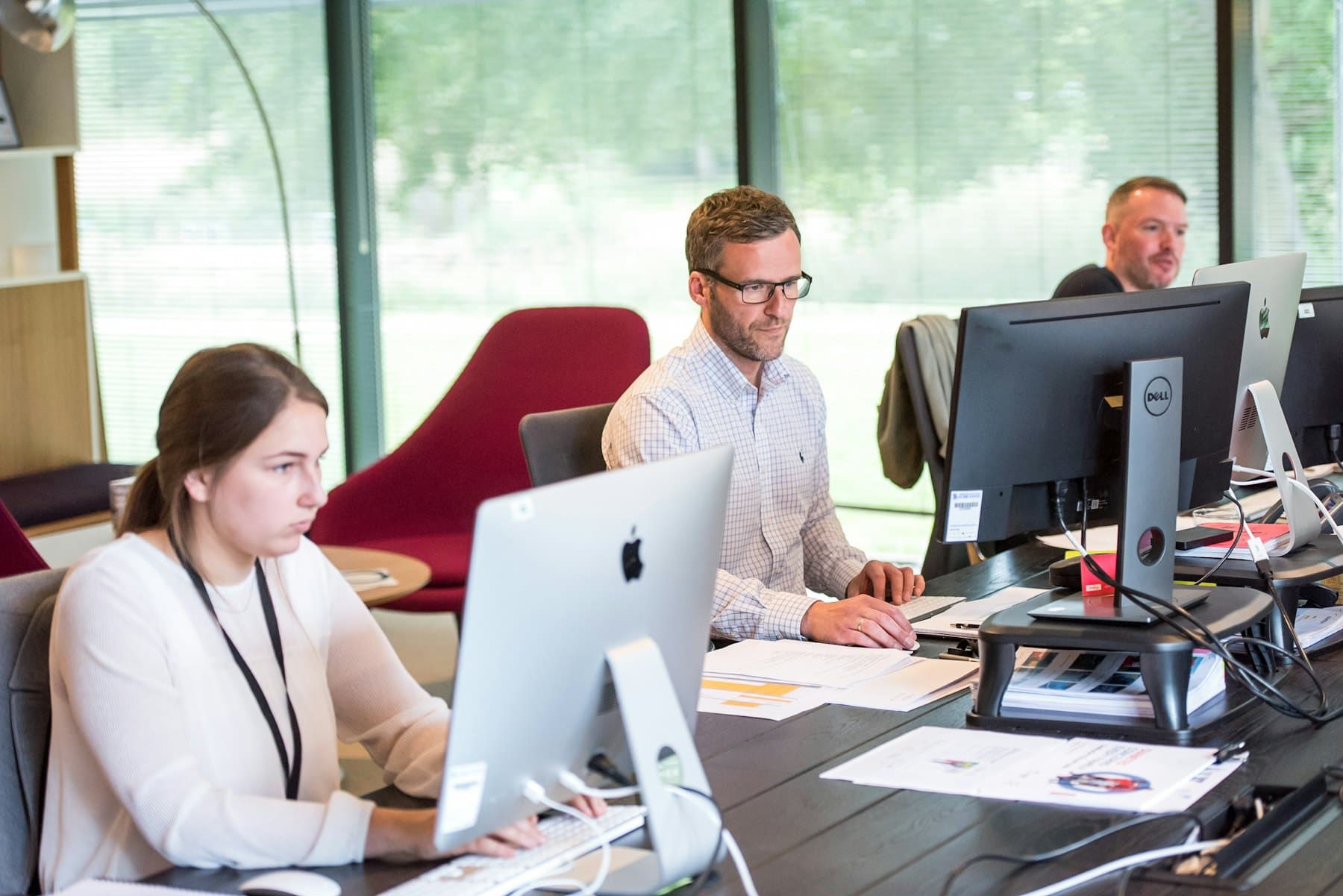 Three people working at computer workstations in a bright office